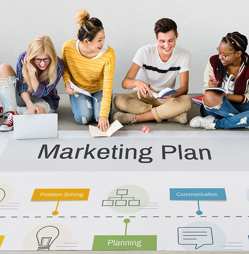 A team of individuals seated on the floor, engaged in discussion over a marketing plan, showcasing collaboration and strategy.